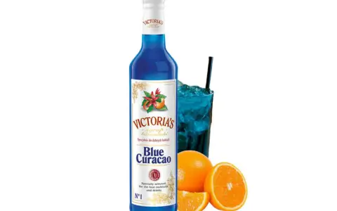 Syrop Blue Curacao Victoria's, idealny do drinków. W szklance niebieski koktajl z lodem i słomką, obok pomarańcze.