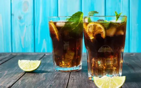 Dwa orzeźwiające drinki z rumem ciemnym, lodem, cytryną i miętą na drewnianym blacie.