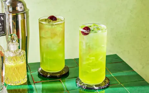 Dwa orzeźwiające drinki Tokyo Ice Tea z wiśniami i lodem, obok shakera i buteleczki z likierem.
