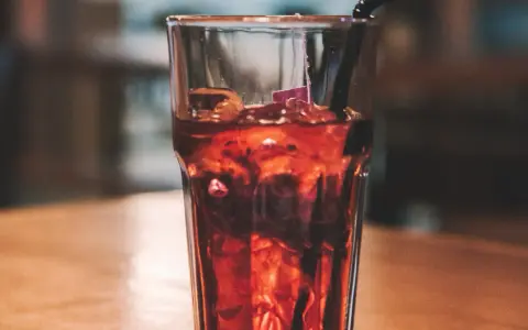 Szklanka z lodem i ciemnym napojem, idealne proporcje whisky z colą. Czarna słomka zanurzona w napoju.