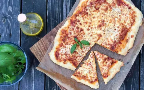 Pyszna pizza margherita z roztopionym serem i świeżą bazylią, obok butelka oliwy i miseczka ziół.