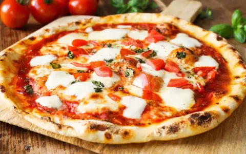 Pyszne ciasto na pizzę bez wyrastania, z pomidorami i mozzarellą, na drewnianej desce.