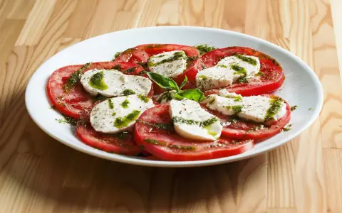 Sałatka caprese z pomidorów i mozzarelli, polana pesto. Idealne zdrowe przekąski na lato.