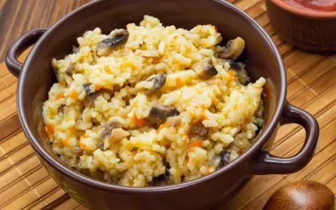 Pyszne risotto z warzywami, pełne grzybów i marchewki, podane w brązowej miseczce.