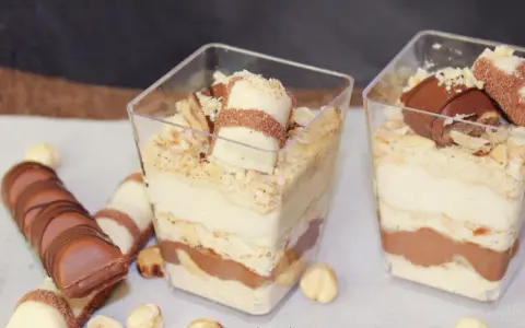 Pyszne ciasto Kinder Bueno w pucharkach, przełożone kremem i czekoladą, posypane orzechami.