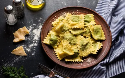 Pyszne ravioli z ricottą i szpinakiem, posypane parmezanem, na brązowym talerzu. Obok kawałki sera i przyprawy.