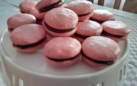 Różowe makaroniki na bezie włoskiej z czekoladowym nadzieniem, ułożone na białej paterze.