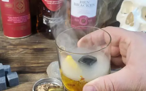 Szklanka z drinkiem otoczona dymem, obok butelki whisky i czaszka. Wyjątkowe drinki z dymem.