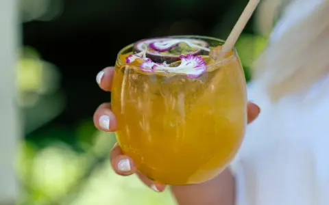 Orzeźwiający drink z marakują, ozdobiony kwiatami i plasterkiem owocu. Idealny na upalne dni.