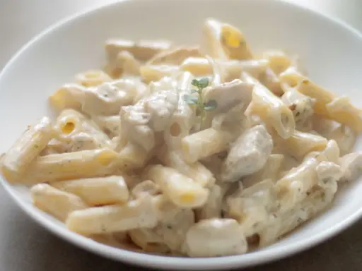 Penne z kurczakiem w kremowym sosie, udekorowane gałązką ziół. Pyszne danie, które zachwyci każdego smakosza.