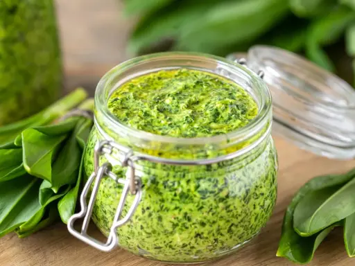 Słoik pełen aromatycznego pesto z czosnku niedźwiedziego, otoczony świeżymi liśćmi tej wiosennej rośliny.