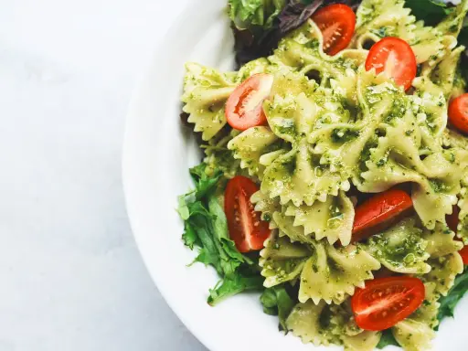 Makaron farfalle z zielonym pesto ze słoika, udekorowany połówkami pomidorków koktajlowych i listkami sałaty.
