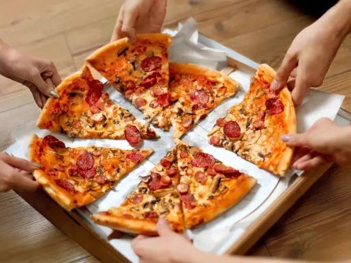 Ręce sięgają po kawałki pysznego ciasta na pizzę z kiełbasą i grzybami.