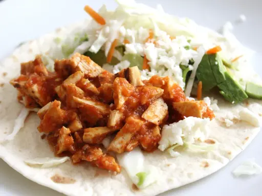 Pyszna tortilla z kurczakiem w sosie, posypana serem feta, z dodatkiem świeżej sałaty i awokado.