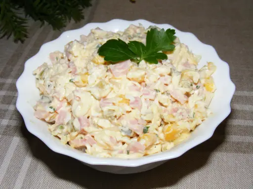 Pyszna sałatka z szynką, jajkiem, kukurydzą i ogórkiem, udekorowana natką pietruszki. Idealna na każdą okazję.
