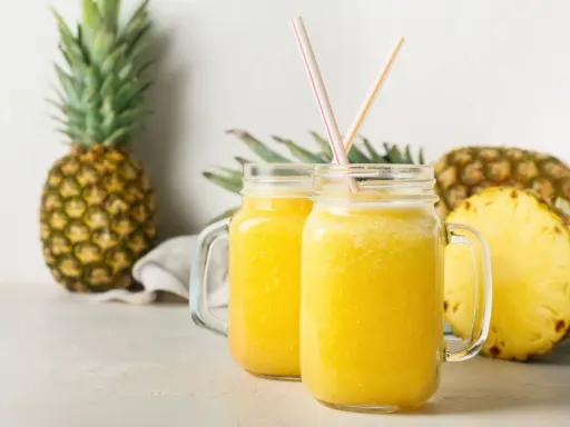 Orzeźwiający drink w ananasie, podany w słoikach, z kawałkami ananasa w tle.