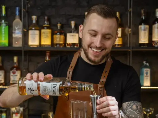 Uśmiechnięty barman, który robi drinki, nalewa whisky Dewar's do jiggera.