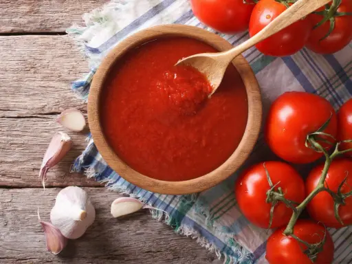 Domowy sos do pizzy z koncentratu, czosnek i świeże pomidory na drewnianym blacie.