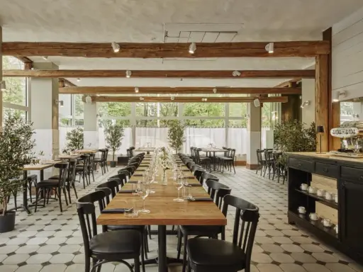 Elegancka sala restauracyjna z długimi stołami, idealna na degustację **primitivo kuchnia i wino**. Drewniane belki i duże okna tworzą przytulną atmosferę.