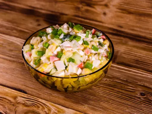 Pyszna sałatka z surimi, z kukurydzą, jajkiem i szczypiorkiem, podana w szklanej misce na drewnianym blacie.