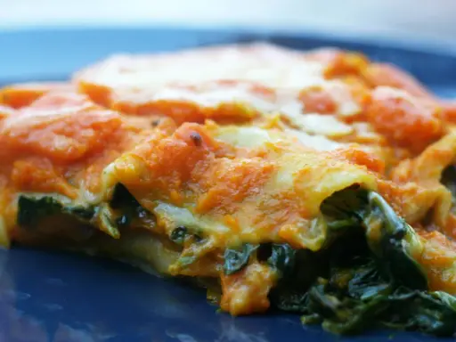 Pyszne lasagne ze szpinakiem, z pomarańczowym sosem i ciągnącym się serem, na granatowym talerzu.