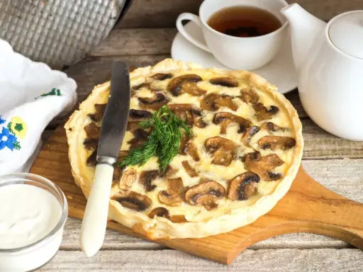 Pyszna tarta z pieczarkami, podana z kubkiem herbaty i śmietaną. Idealna na jesienny obiad.