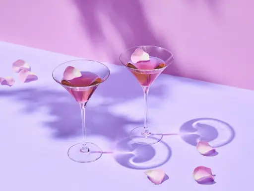 Dwa różowe drinki w kieliszkach do martini, ozdobione płatkami róż. Idealne co do martini na romantyczny wieczór.