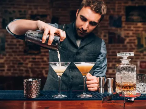 Barman przygotowuje drinki, zastanawiając się, jaki rum do mojito będzie najlepszy. Na blacie stoją kieliszki i karafka z bursztynowym płynem.