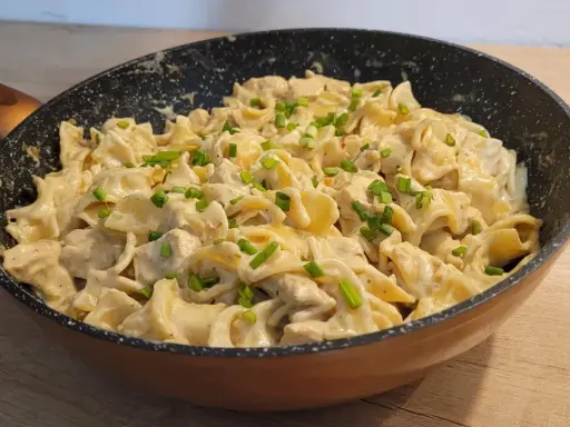Tagliatelle z kurczakiem w sosie śmietanowym, posypane szczypiorkiem, podane w patelni. Pyszne danie gotowe do spożycia.