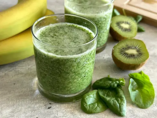 Orzeźwiający koktajl ze szpinakiem, bananami i kiwi. Zielony napój w szklance, obok świeże liście szpinaku i owoce.