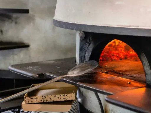 Piec do pizzy z rozżarzonymi węglami. Łopatka czeka, by włożyć do środka pizzę, która będzie piec się w 200 stopniach.