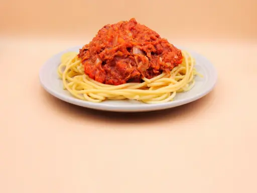 Porcja spaghetti z sosem pomidorowym i tuńczykiem, podana na jasnym talerzu.