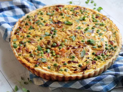 Pyszna tarta z porem i boczkiem, udekorowana groszkiem i ziołami, na niebiesko-białej kratce.