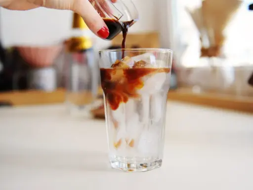 Ręka wylewa espresso na lód w szklance. Idealny napój na upalne dni - tonic espresso.