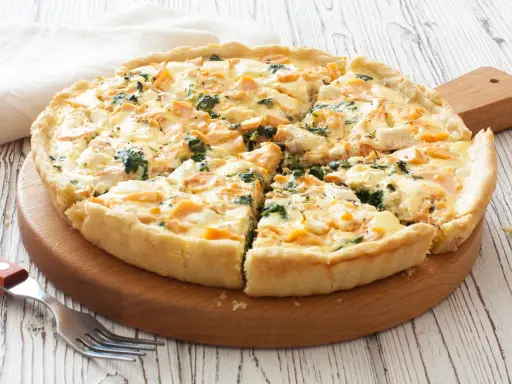 Pyszna tarta z łososiem, szpinakiem i serem feta, pokrojona na kawałki, czeka na talerzu.