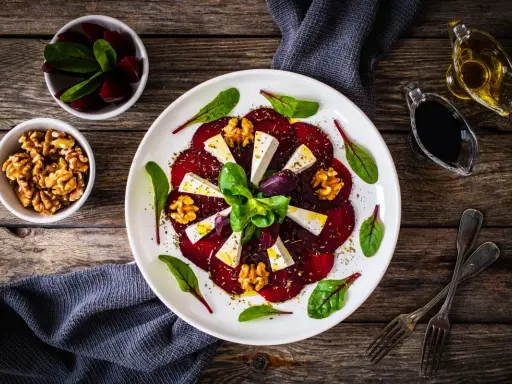 Eleganckie carpaccio z buraka z serem feta, orzechami włoskimi i świeżymi ziołami, podane na białym talerzu.