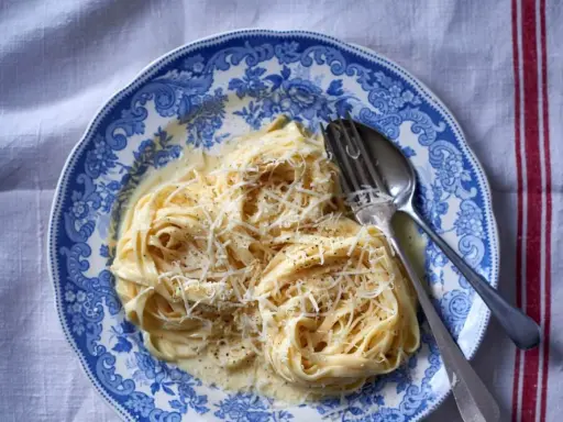 Pyszny makaron alfredo przepis na talerzu z widelcem i łyżką, posypany startym parmezanem.