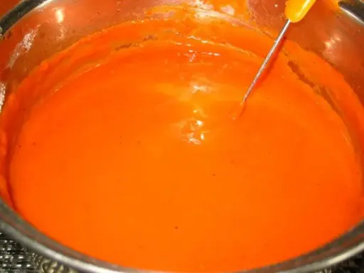 Gęsty, pomarańczowy sos pomidorowy do gołąbków w garnku, z metalową sondą termometru zanurzoną w środku.