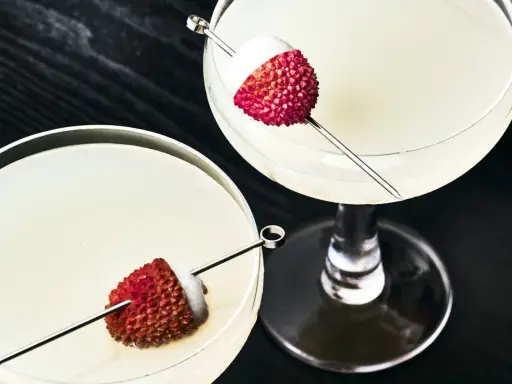 Dwa eleganckie drinki z liczi, ozdobione owocami na patyczkach, kuszą swoim orzeźwiającym wyglądem.
