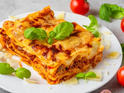 Pyszna, domowa lasagne jak z pieca, z warstwami makaronu, mięsa i sera, ozdobiona świeżą bazylią i parmezanem.