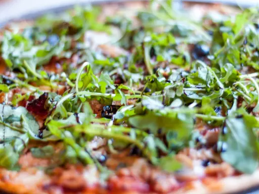 Pyszna pizza z tuńczykiem, rukolą i oliwkami, polana sosem balsamicznym. Idealna na szybki obiad.