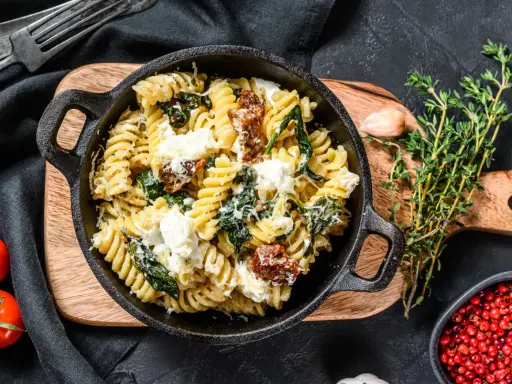 Pyszne fusilli ze szpinakiem i suszonymi pomidorami, posypane parmezanem i kawałkami sera feta.