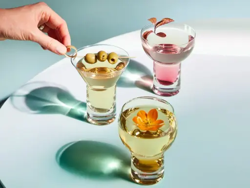 Eleganckie drinki z wódką: martini z oliwkami, różowy koktajl i złoty napój z kwiatem.