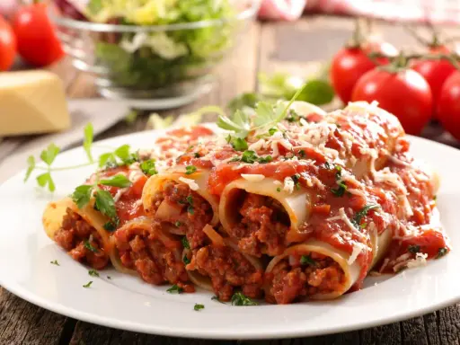 Pyszne cannelloni z mięsem mielonym, polane sosem pomidorowym i posypane parmezanem, na talerzu z pomidorami i sałatką.