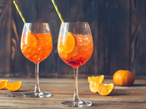 Dwa orzeźwiające drinki z aperolem i sokiem pomarańczowym, ozdobione plasterkami pomarańczy i podane z kolorowymi słomkami. Idealne na letnie popołudnie.