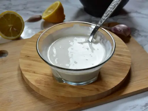 Kremowy sos aioli w szklanej miseczce, obok cytryny i czosnku. Idealny dodatek do dań.