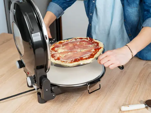 Osoba wkłada pizzę z szynką do okrągłego piekarnika. Idealny moment na pieczenie pizzy w piekarniku!