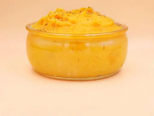 Pomarańczowe puree z batatów w szklanym naczyniu, posypane pieprzem.