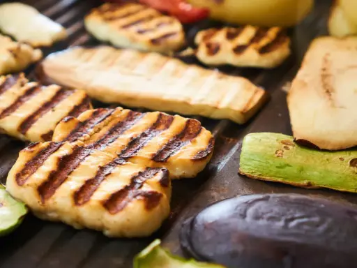 Grillowany ser halloumi z paskami od rusztu, obok cukinia, bakłażan i inne warzywa.