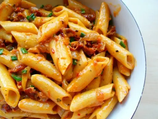 Penne z sosem z suszonych pomidorów i zieloną cebulką, apetyczne danie pełne smaku.